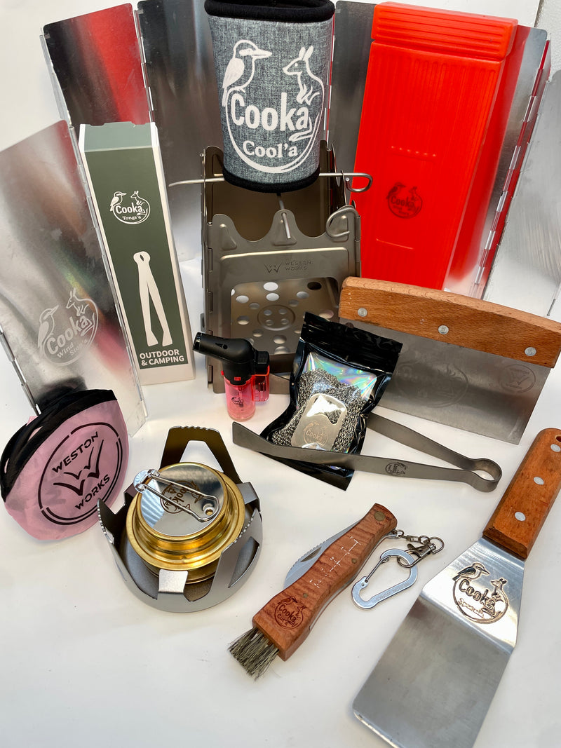 Cooka Crikey Kit laid out: titanium folding stove, Burn'a metho stove, Wind Stop'a, titanium tongs, spatula, Cut'a knife, Wash'a steel mesh scrubber, Cool'a and Frisbee Fire Fan
