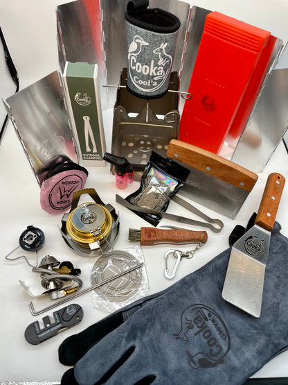 Cooka Big Kahuna Kit laid out: titanium folding stove, Burn'a metho stove, butane adaptor, heat-resistant glove, tongs, spatula, Cut'a knife and Sharpen'a