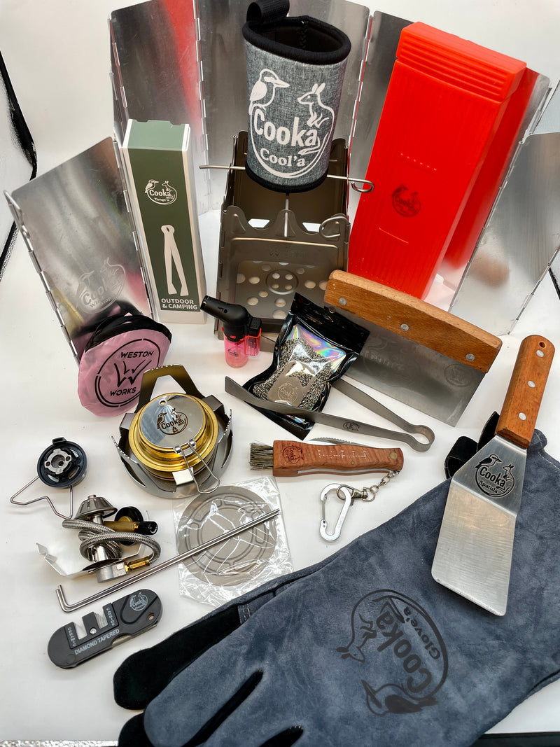 Cooka Big Kahuna Kit laid out: titanium folding stove, Burn'a metho stove, butane adaptor, heat-resistant glove, tongs, spatula, Cut'a knife and Sharpen'a